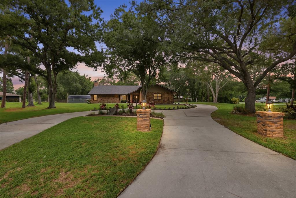 A brick house with a circular driveway and mature trees at dusk — 10616 FOREST RUN DRIVE, BRADENTON, FL