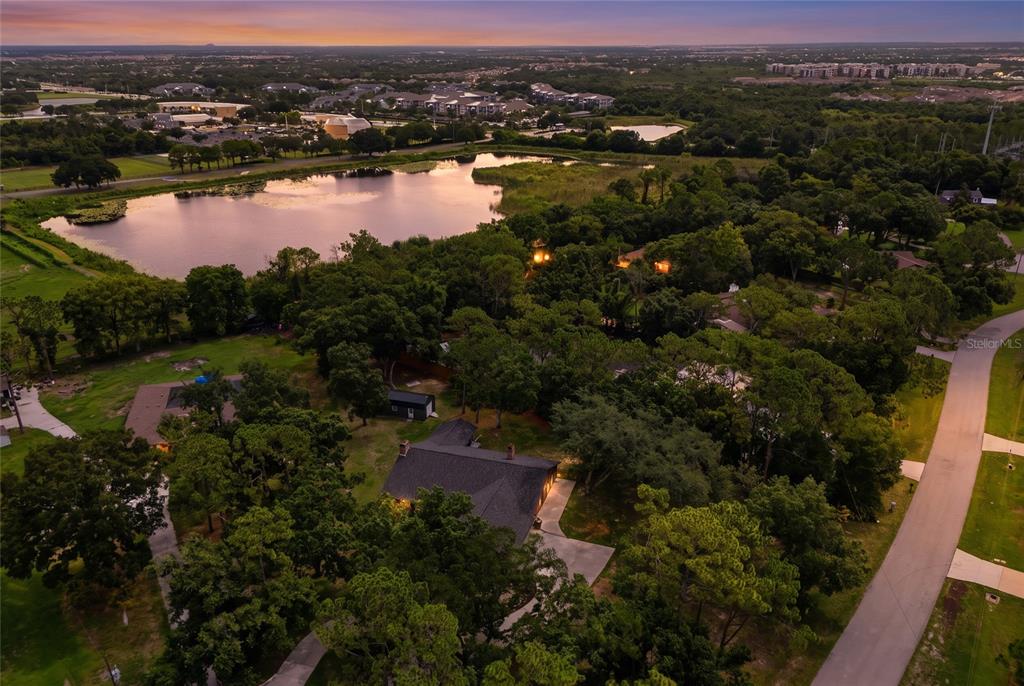 An aerial view shows a house surrounded by trees near a lake at sunset — 10616 FOREST RUN DRIVE, BRADENTON, FL