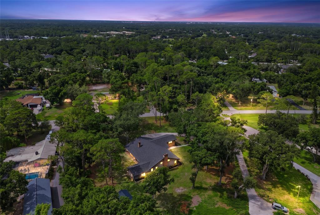 An aerial view shows a house with a dark roof surrounded by trees at dusk — 10616 FOREST RUN DRIVE, BRADENTON, FL