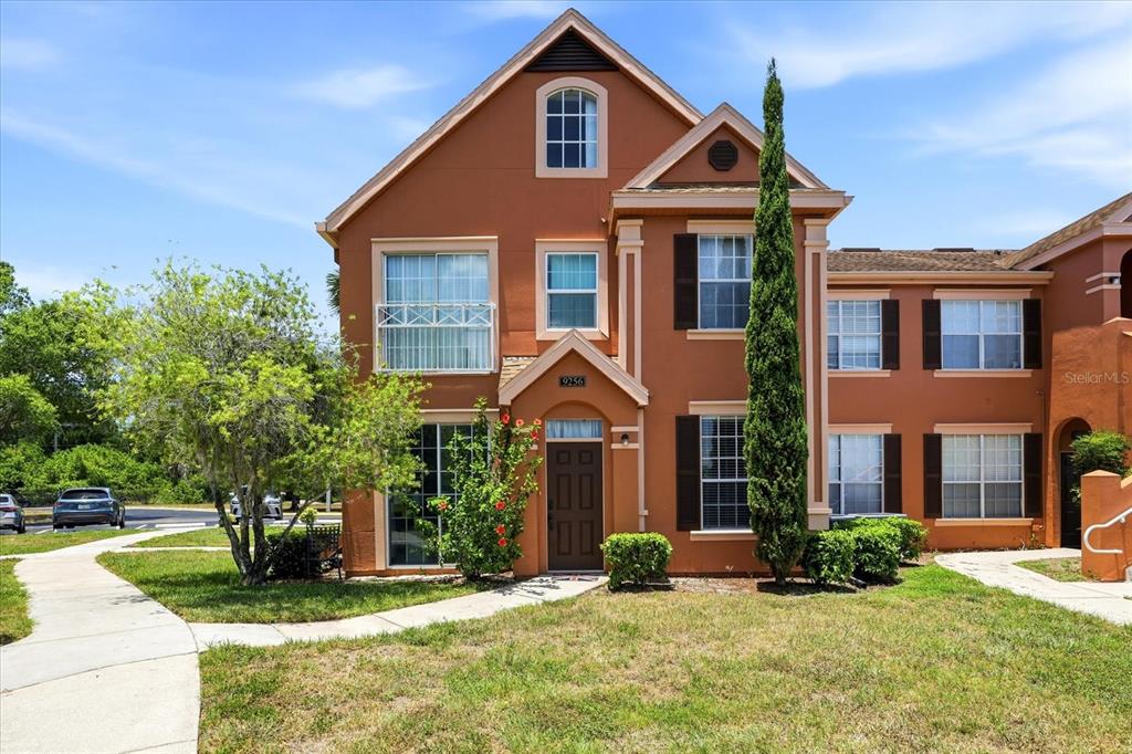 A three-story townhouse with orange stucco siding, dark shutters, and a front walkway — 9256 LAKE CHASE ISLAND WAY, TAMPA, FL
