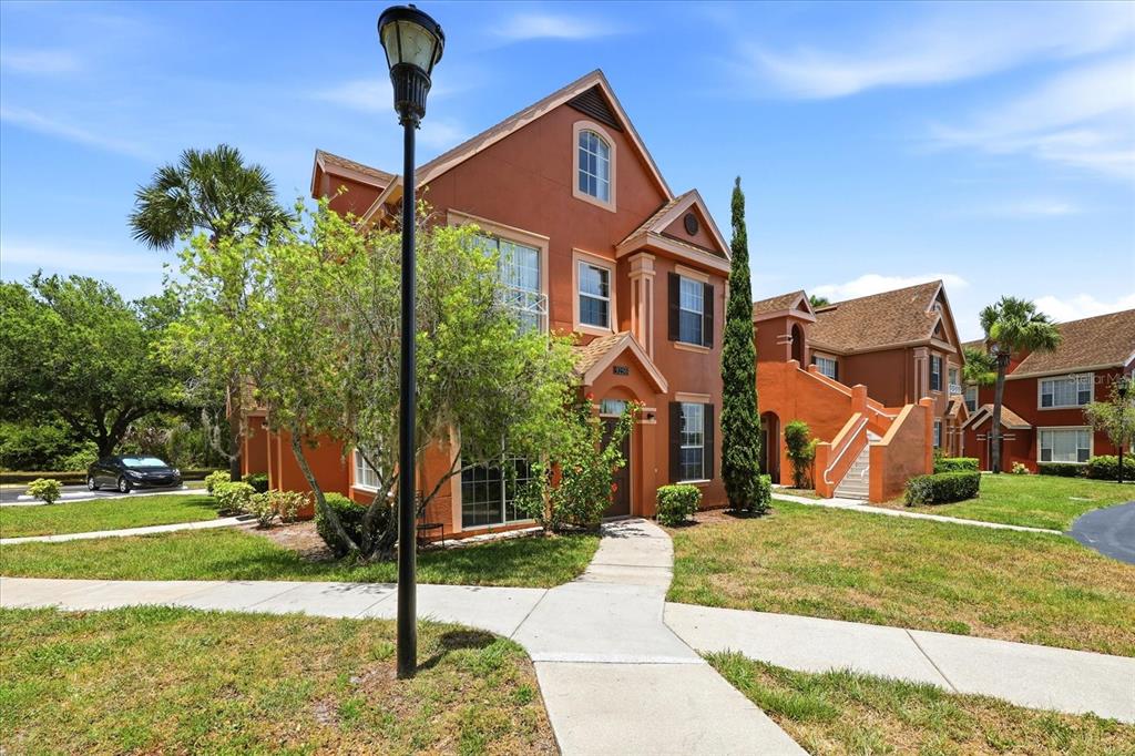 A three-story orange stucco townhouse with a sidewalk and a lamp post in the foreground — 9256 LAKE CHASE ISLAND WAY, TAMPA, FL
