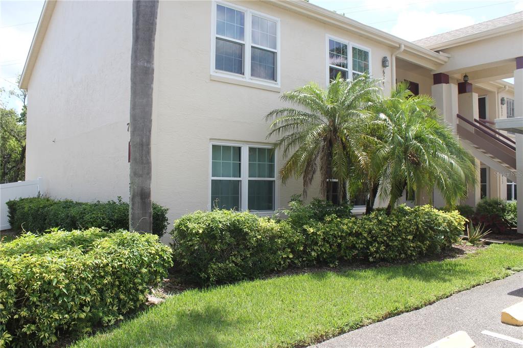 A two-story beige apartment building features palm trees, manicured hedges, and a covered outdoor staircase — 7924 HARDWICK DRIVE UNIT 617, NEW PORT RICHEY, FL