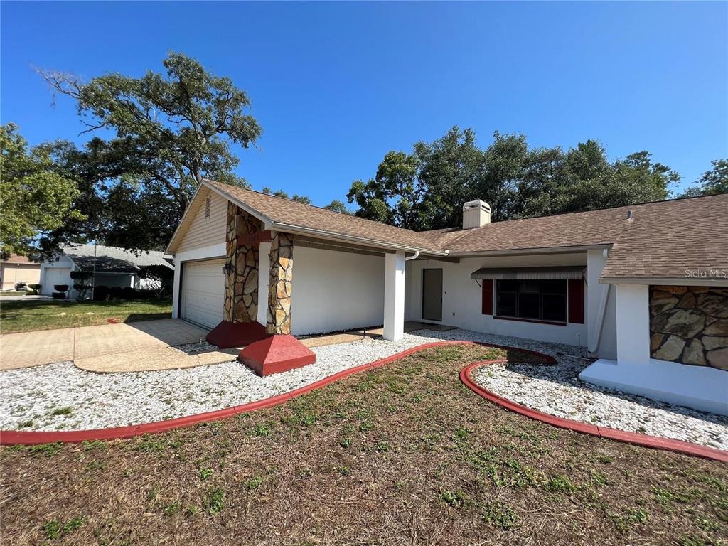 A single-story house with a white exterior, stone accents, and a gravel front yard — 8205 PAGODA DRIVE, SPRING HILL, FL