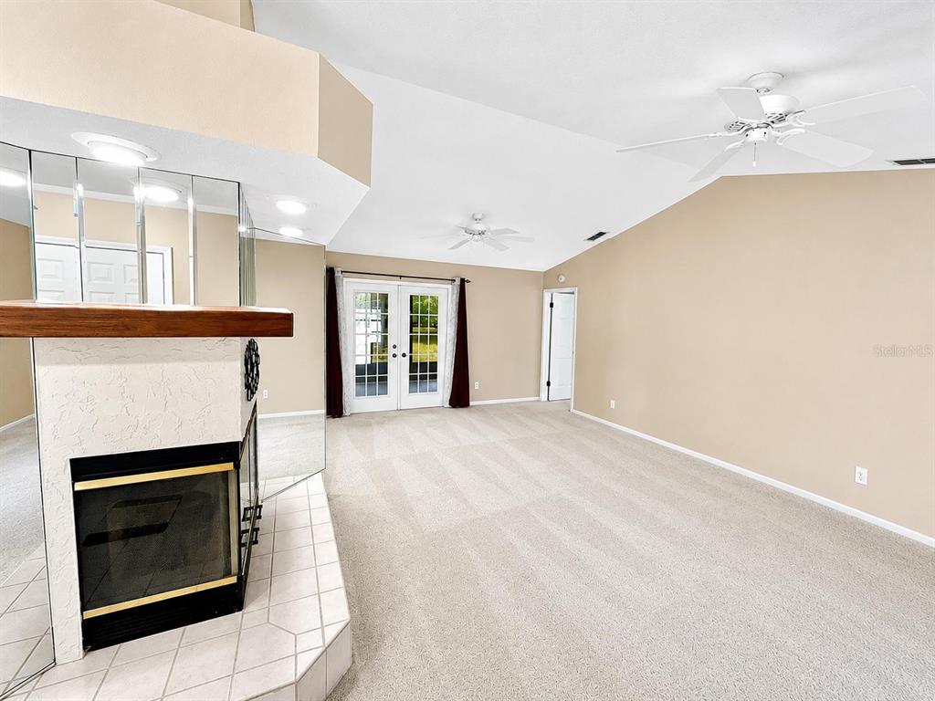 A living room features a fireplace with a mirrored surround, beige carpet, and vaulted ceilings — 8205 PAGODA DRIVE, SPRING HILL, FL