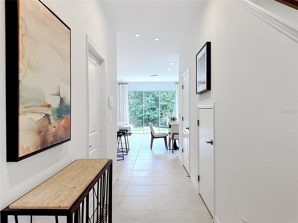 A bright hallway with tile flooring leads toward a dining area and sliding glass doors — 8429 LUNAR SKYE ST, SARASOTA, FL