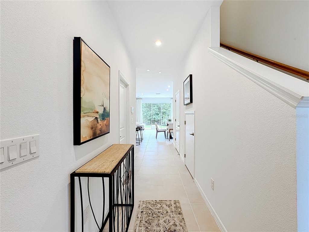 A bright hallway features white walls, tile flooring, a console table, and a staircase — 8429 LUNAR SKYE ST, SARASOTA, FL