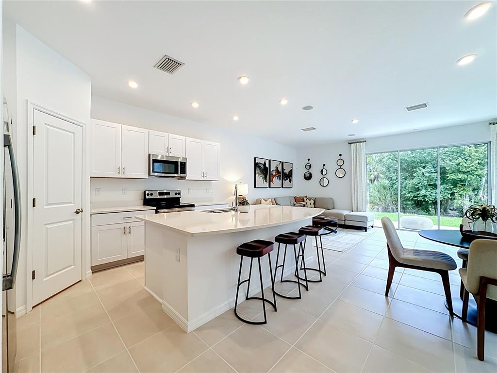 A modern kitchen with white cabinets, a large island, and bar stools opens to a living area — 8429 LUNAR SKYE ST, SARASOTA, FL