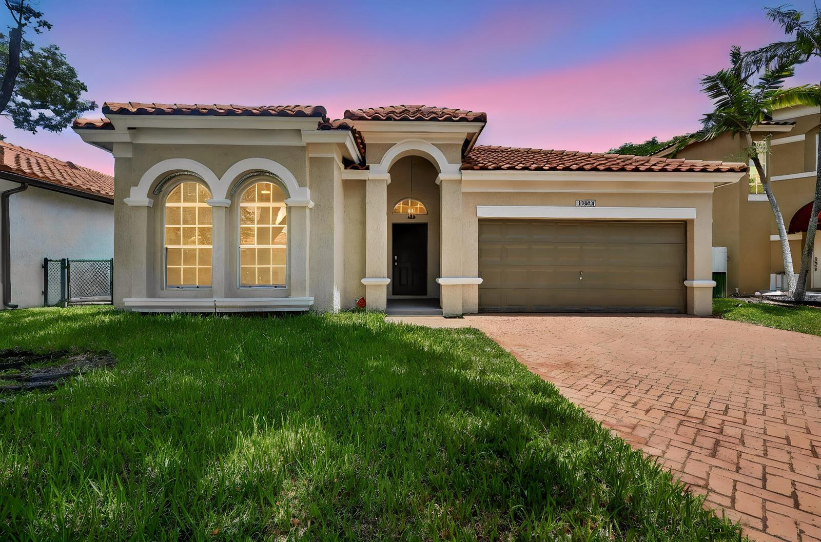 A single-story house with a tiled roof, arched windows, and a paved driveway at dusk — 13844 SW 53rd Street, Miramar FL 33027, MIRAMAR, FL