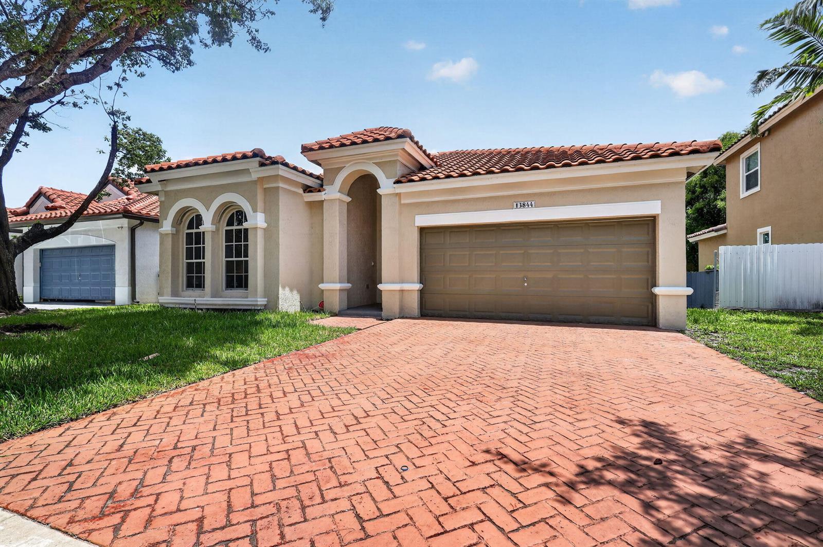 A single-story house with a tan stucco exterior, red tile roof, and brick-paved driveway — 13844 SW 53rd Street, Miramar FL 33027, MIRAMAR, FL