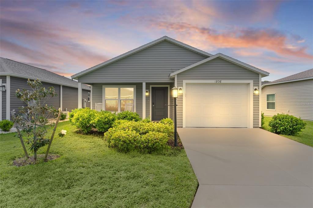 A single-story house with gray siding, a one-car garage, and a landscaped front yard — 1926 HUX COURT, THE VILLAGES, FL