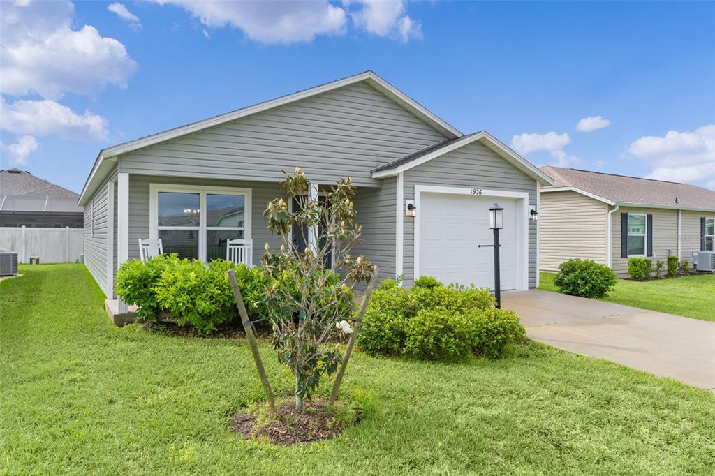 A single-story house with gray horizontal siding, a white garage door, and a front lawn — 1926 HUX COURT, THE VILLAGES, FL