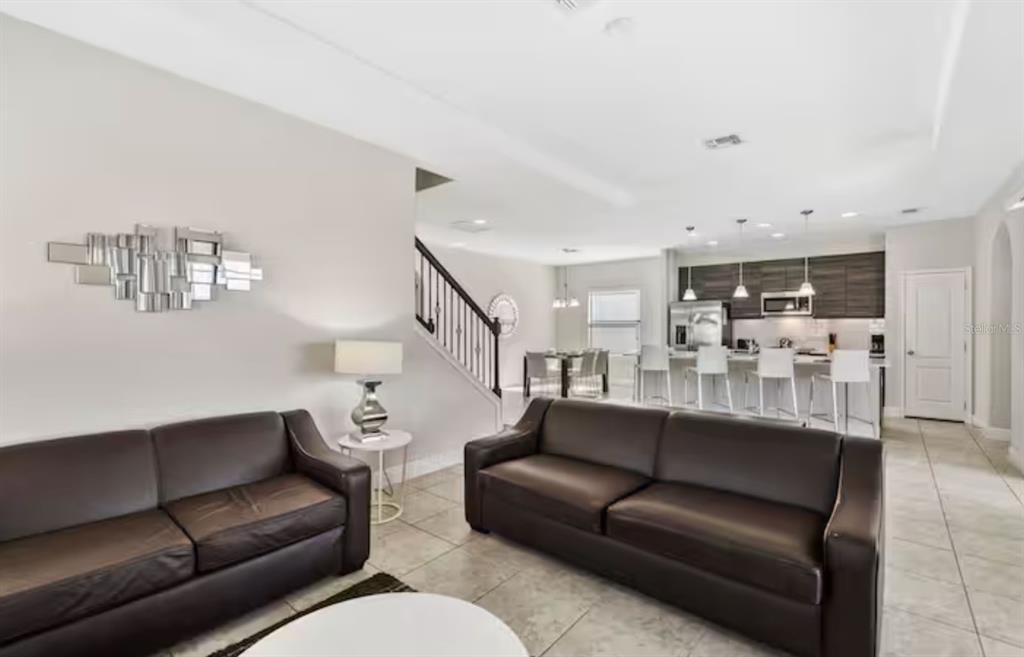 A living room with brown leather sofas, tile floors, and an open kitchen beyond — 167 CLAFFEY COURT, HAINES CITY, FL