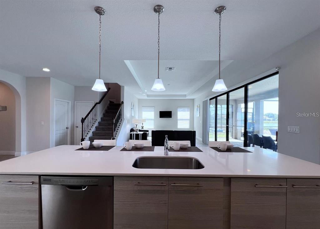 A kitchen island with a sink and pendant lights overlooks a living area and staircase — 167 CLAFFEY COURT, HAINES CITY, FL