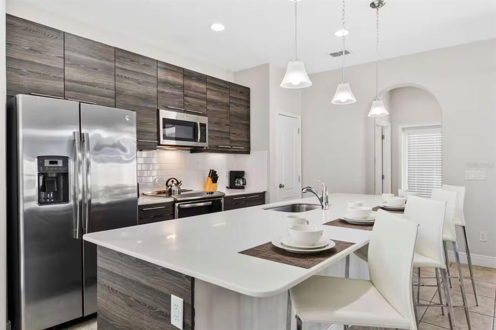 A modern kitchen features dark wood cabinets, stainless steel appliances, and a white quartz island — 167 CLAFFEY COURT, HAINES CITY, FL