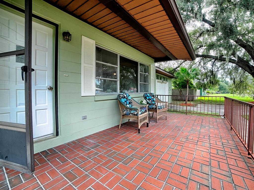 A covered porch with a red brick floor and two wicker chairs sits outside a house — 2269 SOUTHLAND ROAD, MOUNT DORA, FL