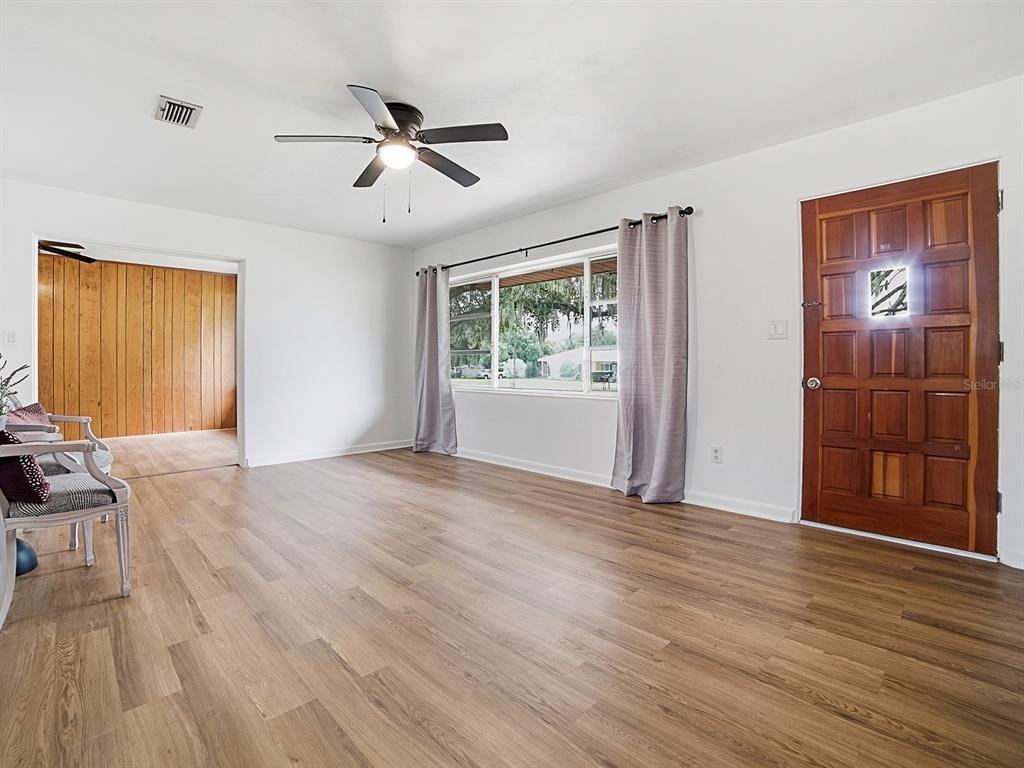 A living room features wood-look flooring, a ceiling fan, a large window, and a wooden door — 2269 SOUTHLAND ROAD, MOUNT DORA, FL