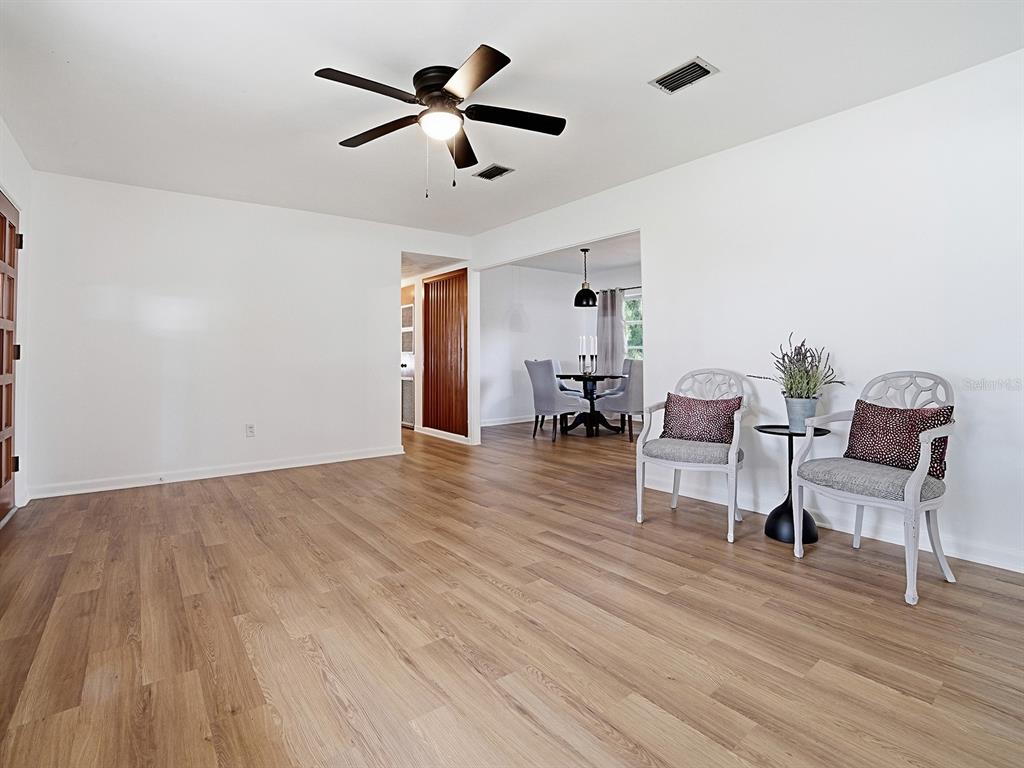 A living room with light wood flooring, a ceiling fan, and two chairs near a dining area — 2269 SOUTHLAND ROAD, MOUNT DORA, FL