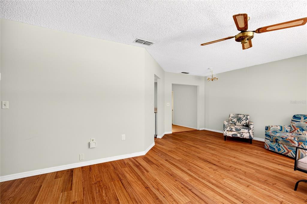 A living room with wood-look flooring, a ceiling fan, and two patterned armchairs — 9021 SW 108TH PLACE, OCALA, FL