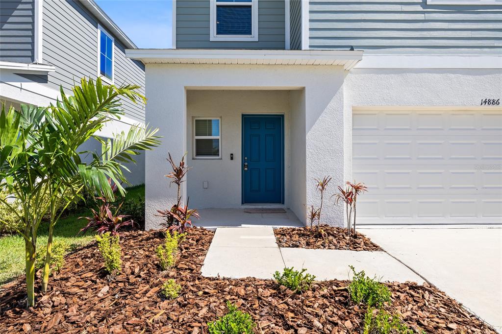 The exterior of a house features a blue front door, white stucco, and a garage — 14886 SUMMER BRANCH DRIVE, LITHIA, FL
