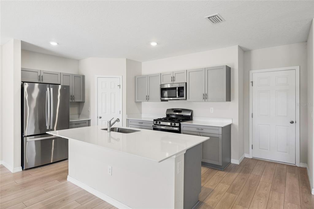 A kitchen features gray cabinets, stainless steel appliances, a white island, and light wood flooring — 14886 SUMMER BRANCH DRIVE, LITHIA, FL