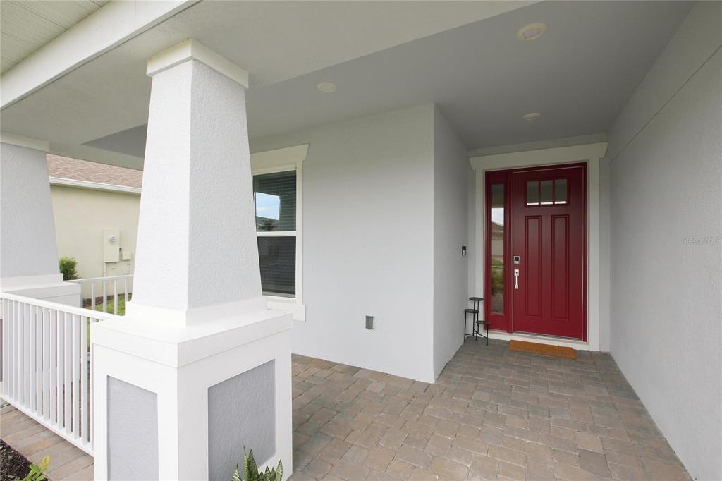 A covered front porch features a red door, white columns, and paver flooring — 1633 REMINGTON TRACE DRIVE, PORT CHARLOTTE, FL