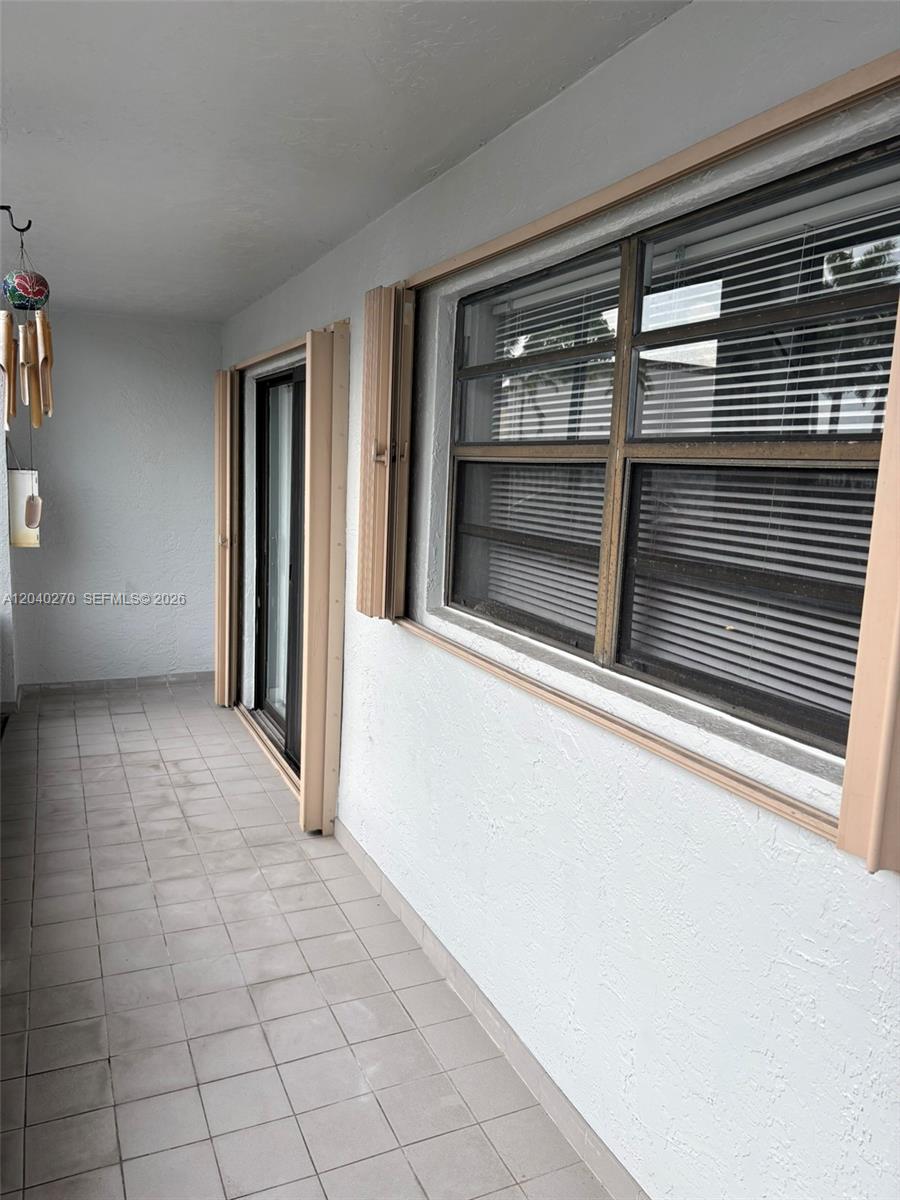 A covered outdoor patio features light-colored tile flooring, white stucco walls, and accordion hurricane shutters — 18350 Mediterranean Blvd # 27, Hialeah FL 33015, HIALEAH, FL