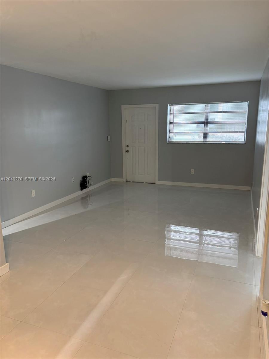 An empty room features light gray walls, large white floor tiles, and a single window — 18350 Mediterranean Blvd # 27, Hialeah FL 33015, HIALEAH, FL