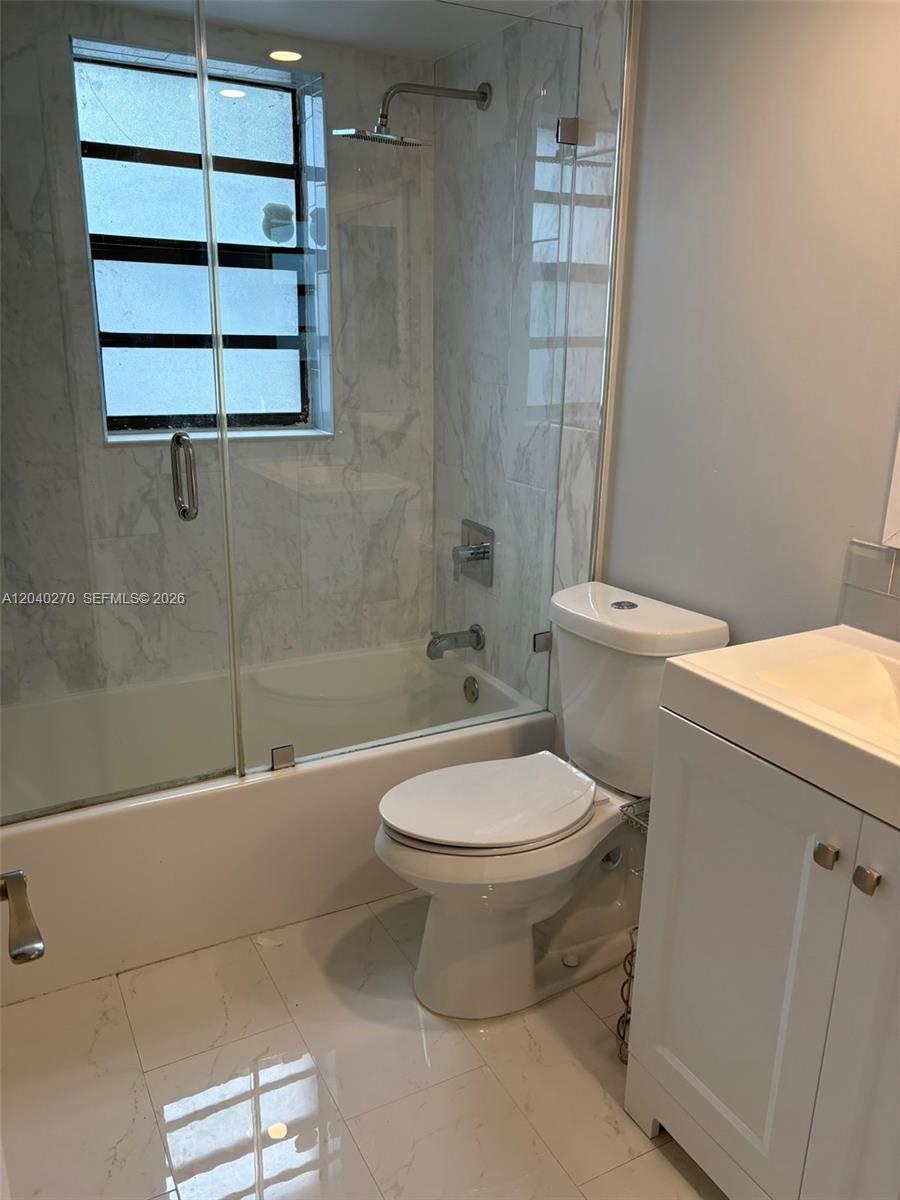 A bathroom features a white vanity, a toilet, and a glass-enclosed tub with marble-look tile — 18350 Mediterranean Blvd # 27, Hialeah FL 33015, HIALEAH, FL