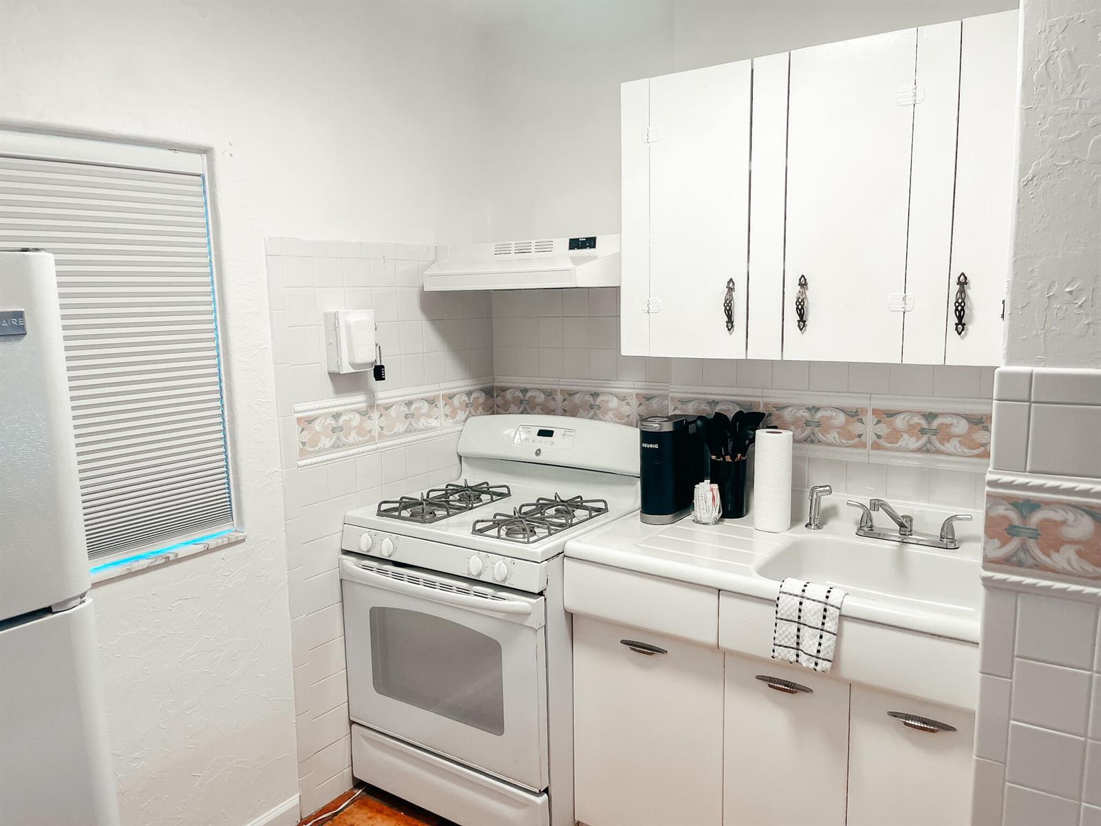 A small kitchen features white cabinets, a gas stove, a sink, and tiled walls — 516 3rd Avenue S, FL 33460, FL