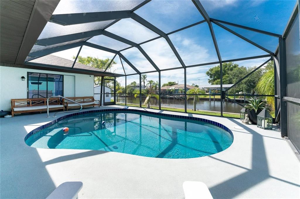 A screened-in pool patio overlooks a canal with a wooden bench along the house wall — 12420 MINOT AVENUE, PORT CHARLOTTE, FL