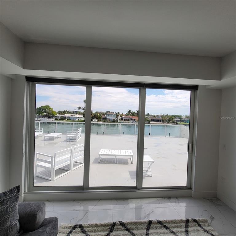 A room with white marble floors looks out through sliding glass doors onto a waterfront terrace — 415 ISLAND WAY UNIT 206, CLEARWATER BEACH, FL