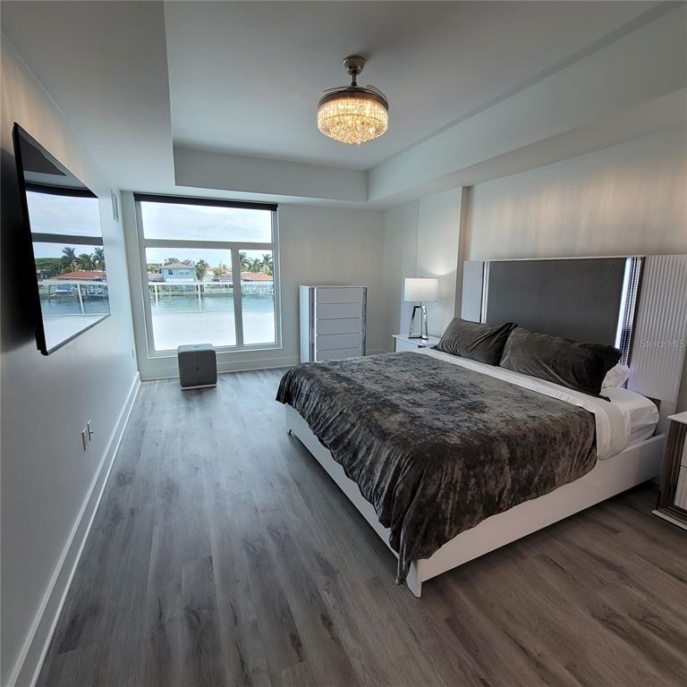 A modern bedroom features a king bed, gray wood flooring, and a waterfront window view — 415 ISLAND WAY UNIT 206, CLEARWATER BEACH, FL