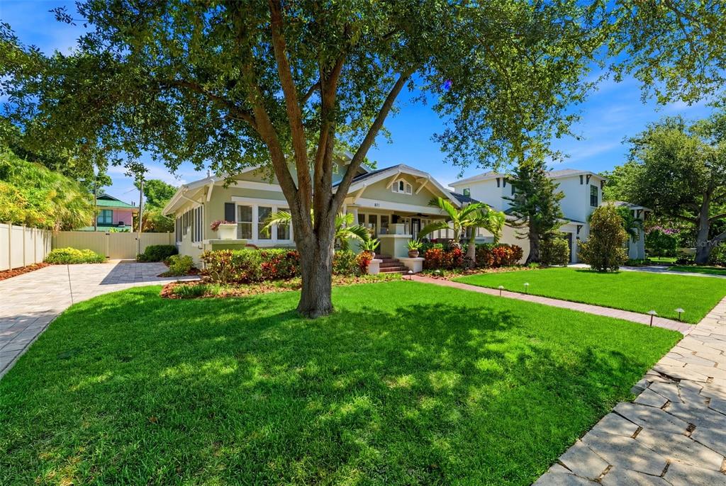 A green bungalow with a front porch and large tree stands behind a manicured lawn — 871 17TH AVENUE N, ST PETERSBURG, FL