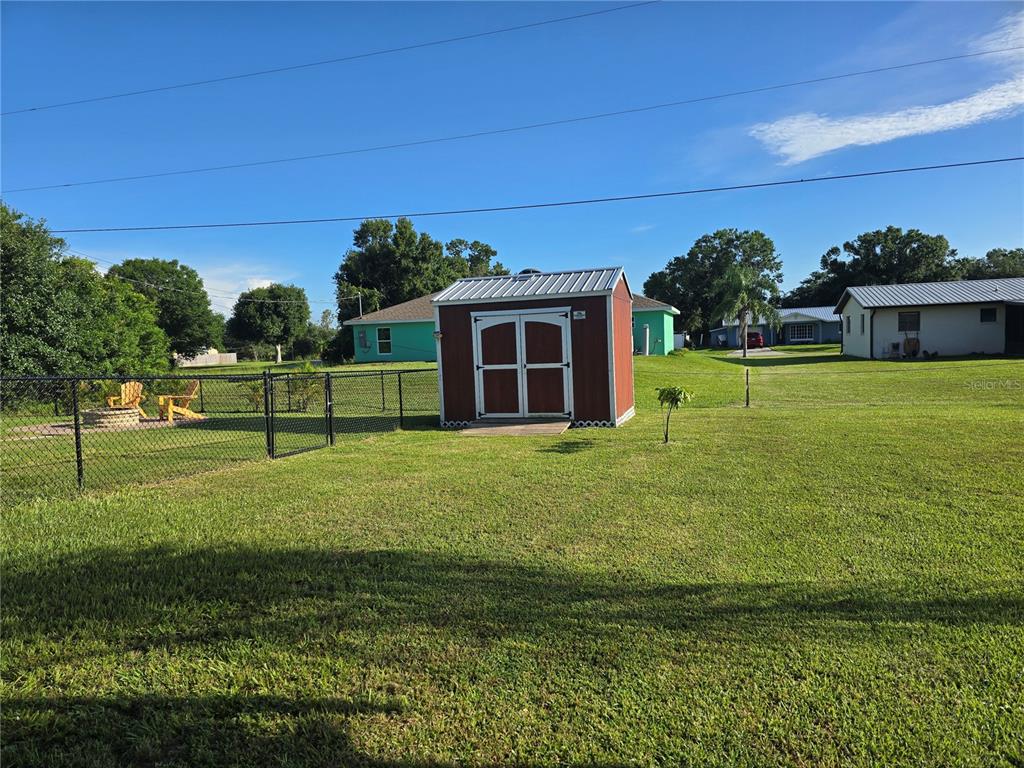 A red storage shed sits in a large, fenced-in grassy backyard under a blue sky — 7182 SW BIRD ROAD, ARCADIA, FL