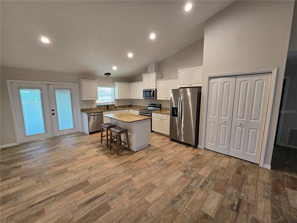 A kitchen features white cabinets, granite countertops, stainless steel appliances, and wood-look tile flooring — 7182 SW BIRD ROAD, ARCADIA, FL