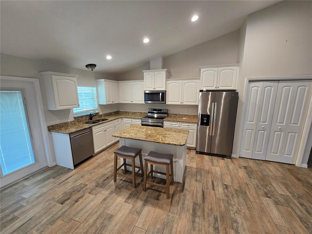 A kitchen features white cabinets, granite countertops, stainless steel appliances, a center island, and wood-look flooring — 7182 SW BIRD ROAD, ARCADIA, FL