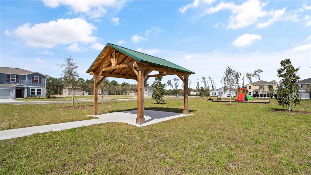 A wooden pavilion with a green metal roof stands in a grassy neighborhood park — 1367 BLUE ASH LANE, DELAND, FL