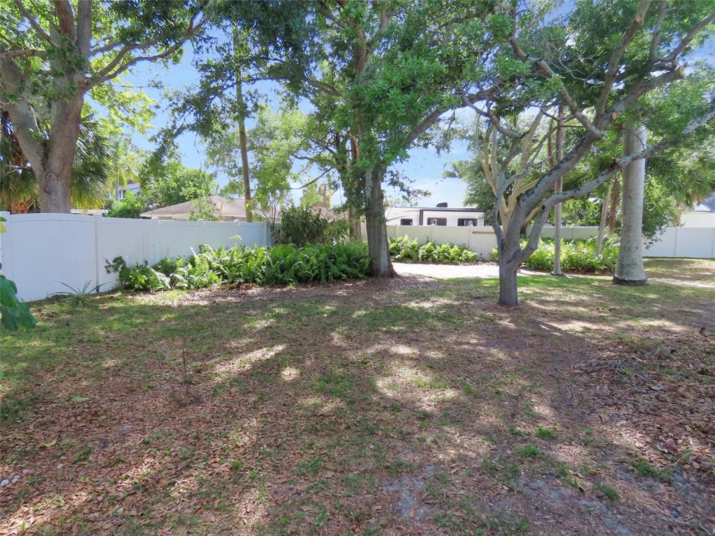 A grassy backyard features mature trees, a white vinyl fence, and a patch of ferns — 408 27TH STREET W, BRADENTON, FL