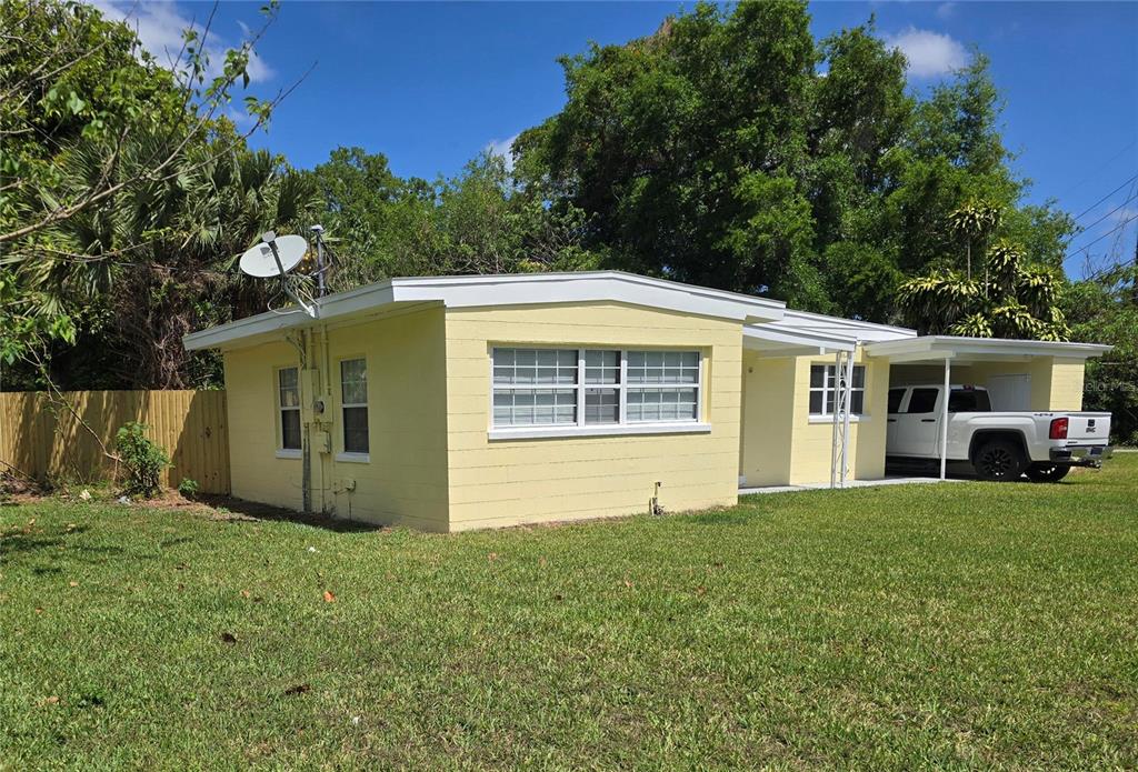 A single-story yellow concrete block house with a white carport and a satellite dish — 5825 YUCATAN DRIVE, ORLANDO, FL