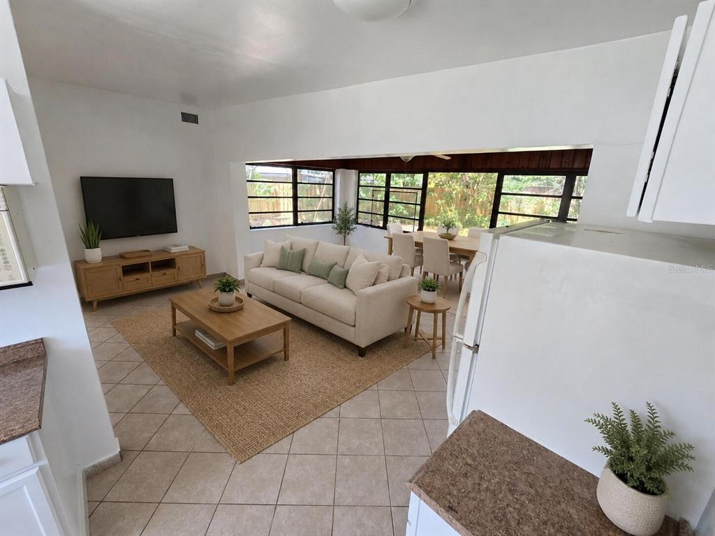 A living room with a beige sofa, coffee table, and dining area featuring large windows — 5825 YUCATAN DRIVE, ORLANDO, FL