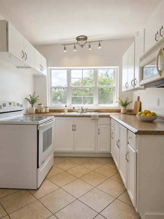 A kitchen with white cabinets, tan countertops, tile flooring, and a window above the sink — 5825 YUCATAN DRIVE, ORLANDO, FL