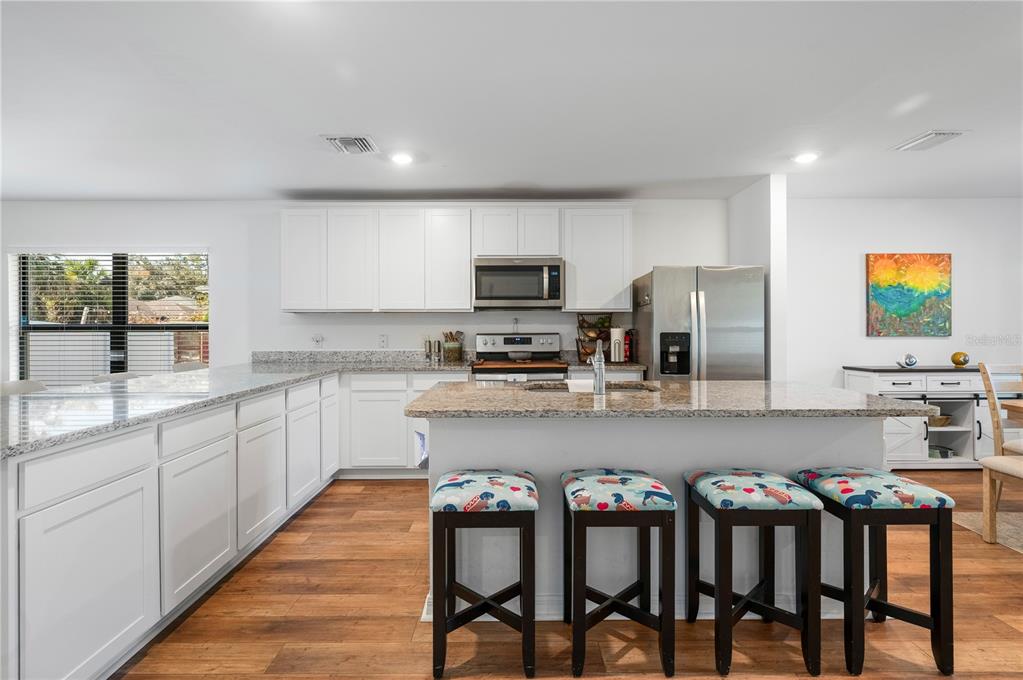 A kitchen with white cabinets, granite countertops, a breakfast bar, and wood-look flooring — 3638 WENTWORTH STREET, NORTH PORT, FL