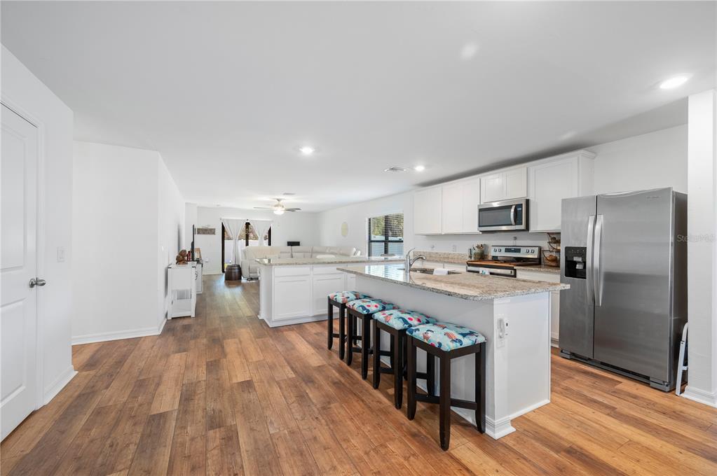 A kitchen with white cabinets, granite countertops, and stainless steel appliances overlooks a living area — 3638 WENTWORTH STREET, NORTH PORT, FL