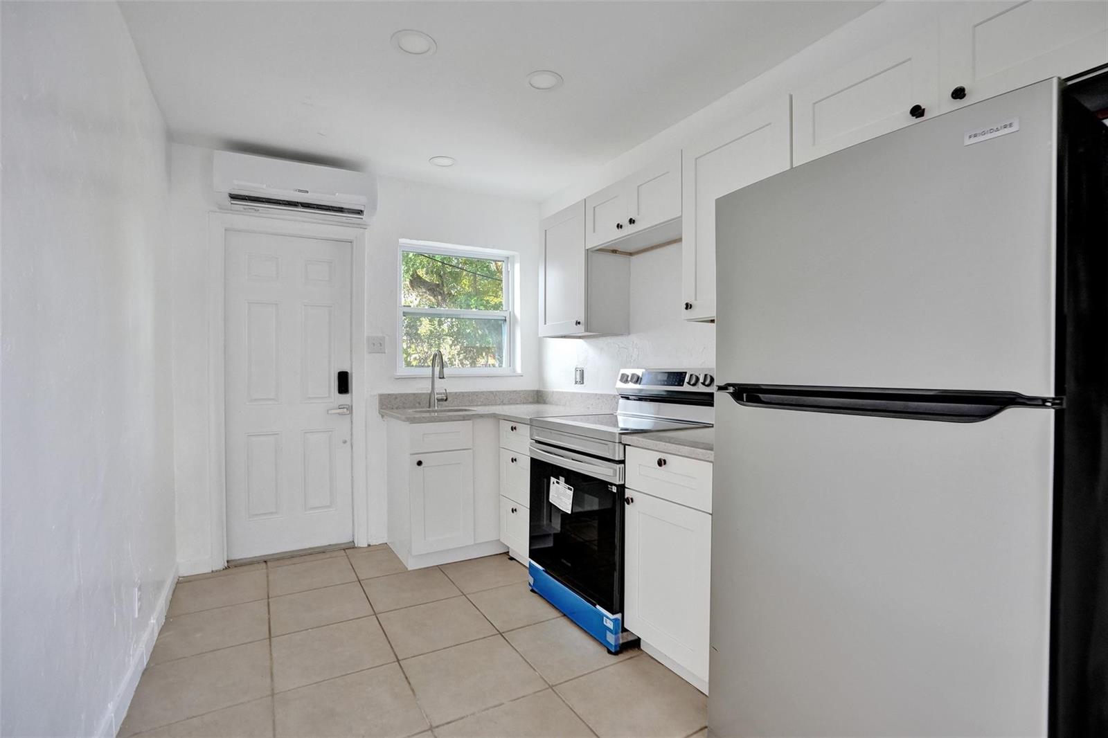 A kitchen features white cabinets, stainless steel appliances, tile flooring, and a door to outside — 306 NE 13th Avenue, Pompano Beach FL 33060, POMPANO BEACH, FL