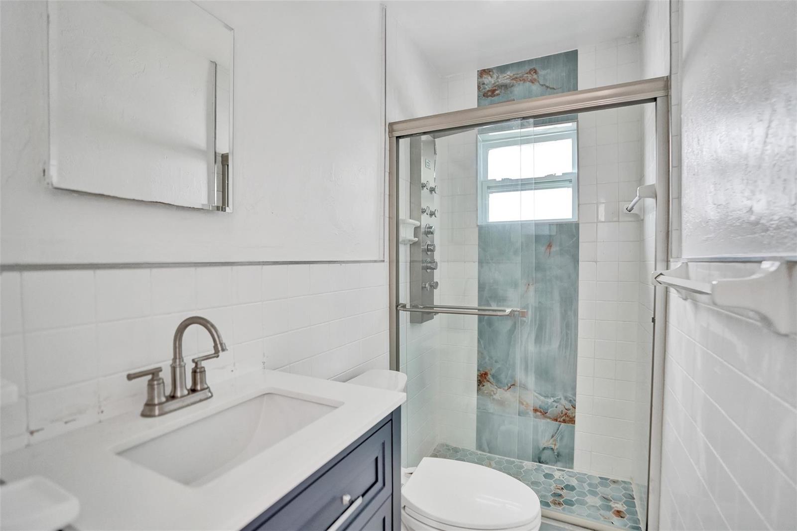 A bathroom features a blue vanity, white subway tile walls, and a glass-enclosed shower — 306 NE 13th Avenue, Pompano Beach FL 33060, POMPANO BEACH, FL