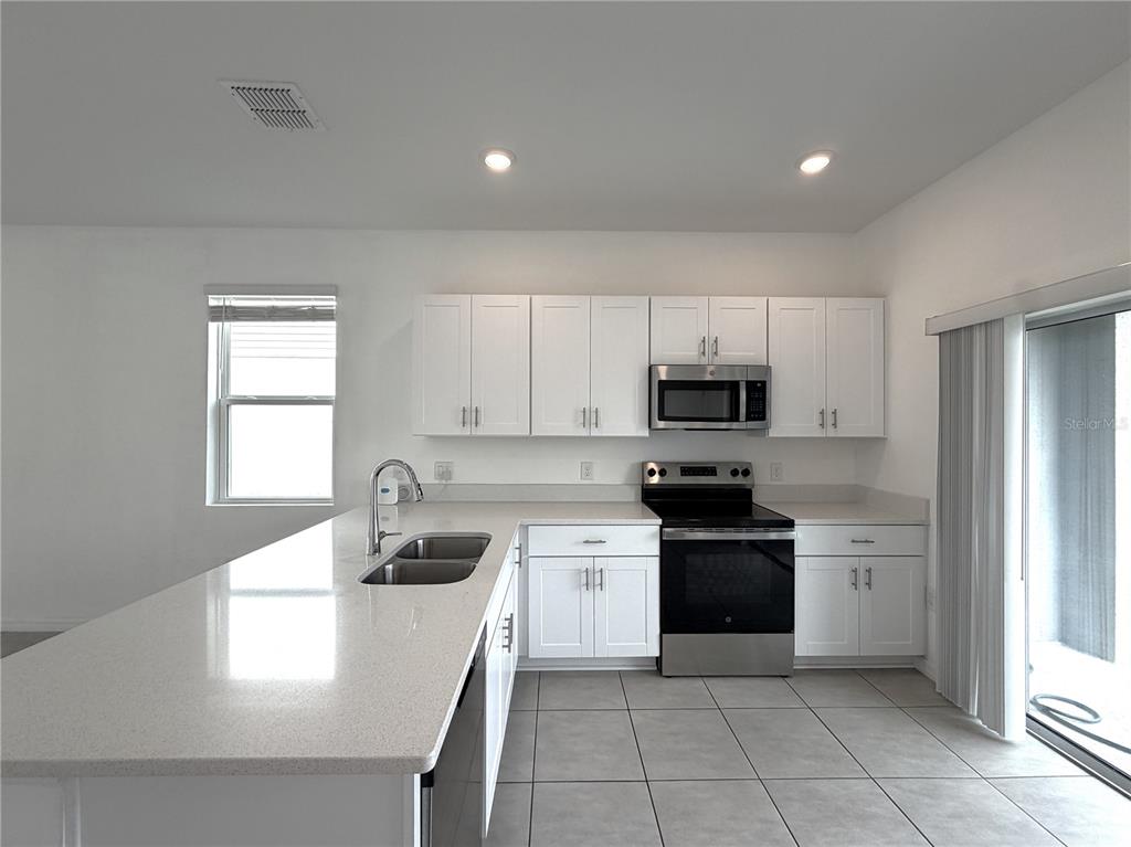 A kitchen features white cabinets, stainless steel appliances, quartz countertops, and light-colored tile flooring — 3187 SKYLINE LOOP, POINCIANA, FL