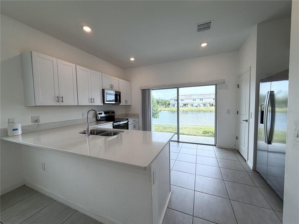 A kitchen with white cabinets, quartz countertops, stainless steel appliances, and a view of water — 3187 SKYLINE LOOP, POINCIANA, FL