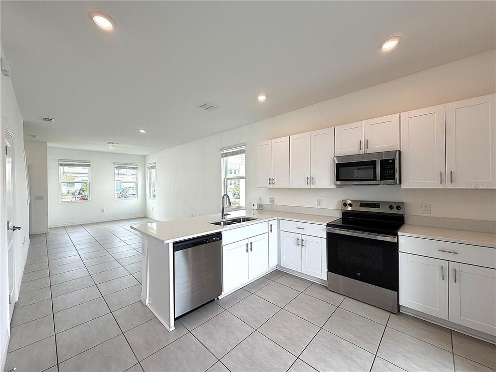 A kitchen with white cabinets, stainless steel appliances, and tile flooring opens to a living area — 3187 SKYLINE LOOP, POINCIANA, FL