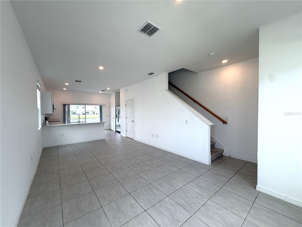 This open-concept living area features light tile flooring, a staircase, and a kitchen background — 3187 SKYLINE LOOP, POINCIANA, FL