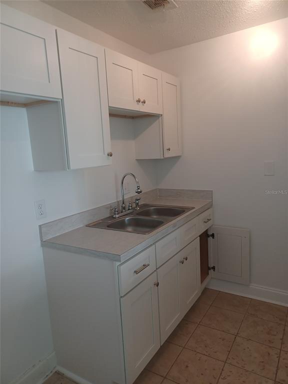 A kitchen features white cabinets, a double-basin stainless steel sink, and light-colored tile flooring — 245 S MCMULLEN BOOTH ROAD UNIT 17, CLEARWATER, FL